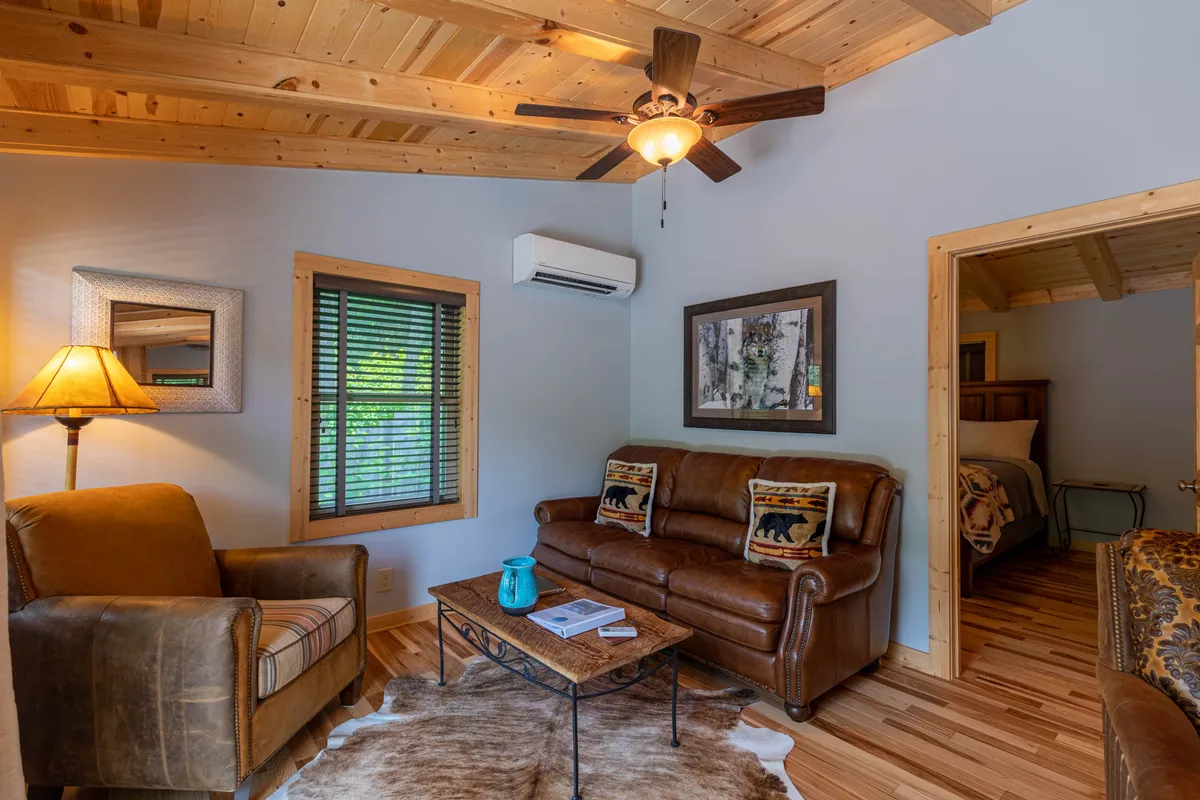 This image centers on a leather couch adorned with bear-themed pillows, a wooden coffee table, and warm lighting. The décor feels comfortable and thoughtfully curated, with elements that invite guests to unwind after a day’s adventure. The space exudes a homey, relaxed vibe and is perfect for socializing or simply enjoying a quiet moment.