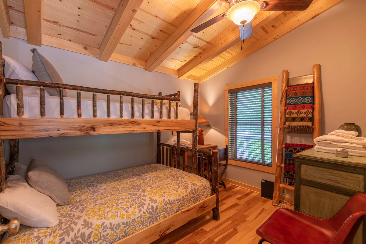 A warm and welcoming bedroom with built-in bunk beds, wooden accents, soft textiles, and a window with blinds. The space feels designed for families, offering comfort, togetherness, and a view outside for a connection to nature.