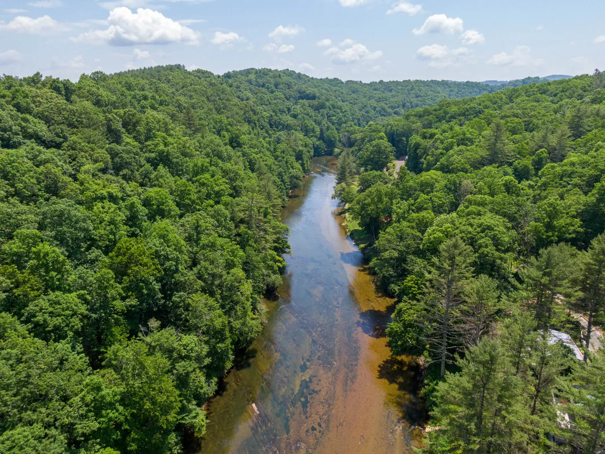 This image features a tranquil view of the South Fork New River winding through dense forest and rolling hills. The river is easily visible, suggesting opportunities for kayaking, tubing, or fishing, while the surrounding landscape highlights the area's natural beauty and potential for hiking and wildlife observation.