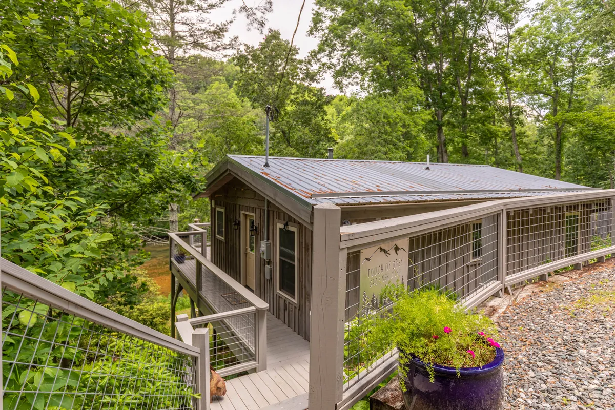 A welcoming exterior shot of the cabin entrance, surrounded by lush greenery and vibrant potted flowers. The setting hints at easy access to nature, making it an ideal starting point for hikes or river excursions.