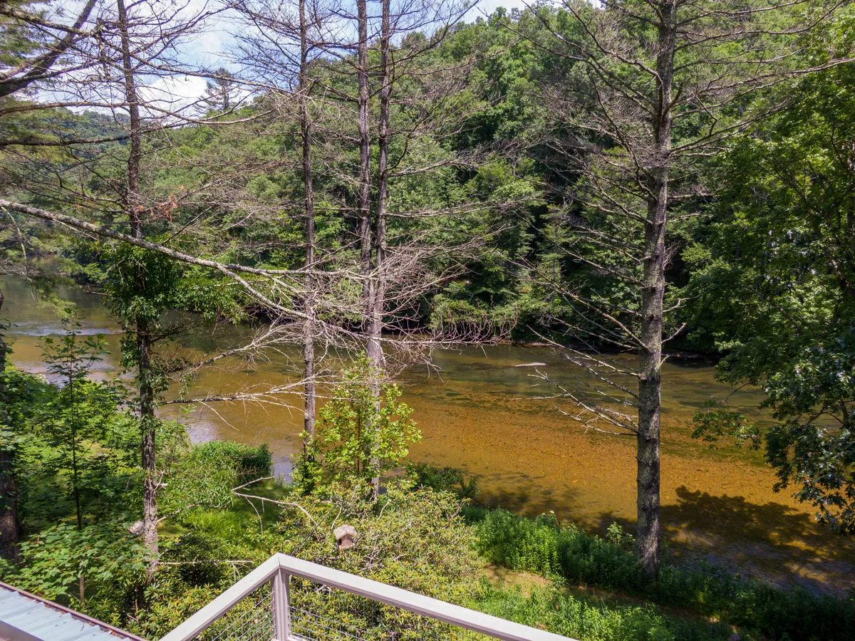 A tranquil scene featuring the calm river flanked by lush green trees, with dappled sunlight shimmering on the water. The image captures the essence of early morning or late afternoon, inviting viewers to imagine relaxing by the riverbank. Activities like fishing, kayaking, and birdwatching naturally fit into the setting.