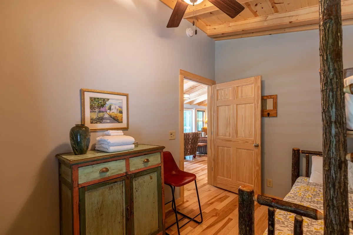 A cozy interior corner featuring a wooden dresser, framed artwork, a vibrant red chair, and an open door that hints at functional storage spaces. The scene suggests comfort and convenience, with enough space to relax or manage daily routines like laundry.