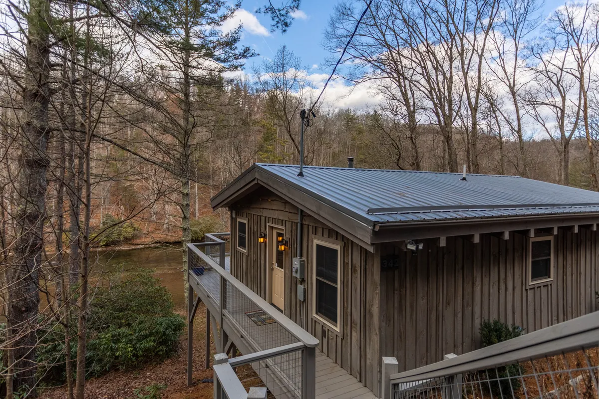 A peaceful view of a wooden cabin surrounded by trees and the river in the background. The scenery blends the cabin's rustic charm with its prime location for nature observation and river access.