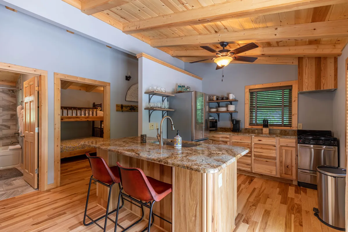 This image shows a welcoming kitchen space centered around a granite-topped island. Warm wooden cabinets line the walls, complemented by bar stools that encourage casual gatherings or quick breakfasts. The kitchen is bright and inviting, creating a space for culinary activities and socializing.
